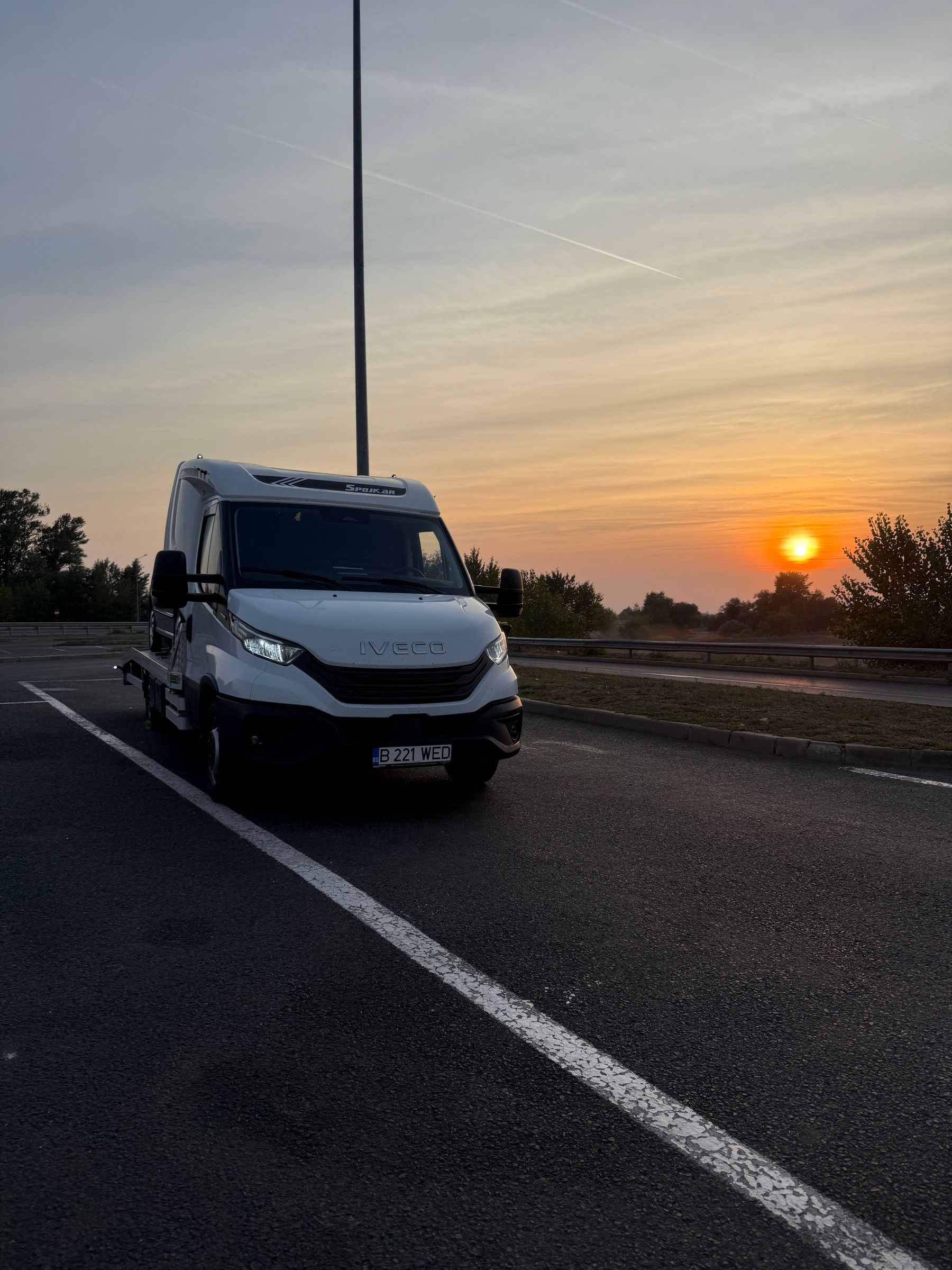 Autoplatformă Diava Cars Iveco Daily oprită pe autostradă la apus, cu un autoturism încărcat